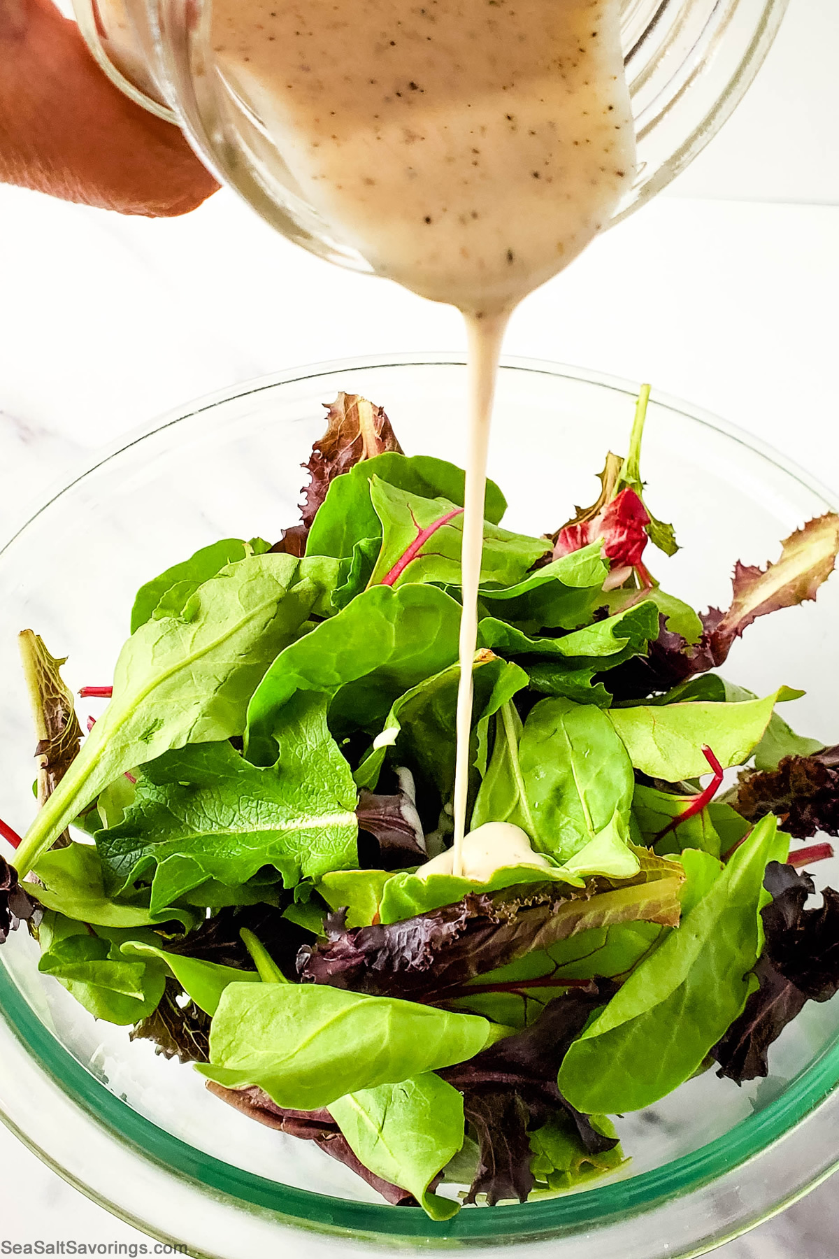 pouring dressing on top of leafy greens