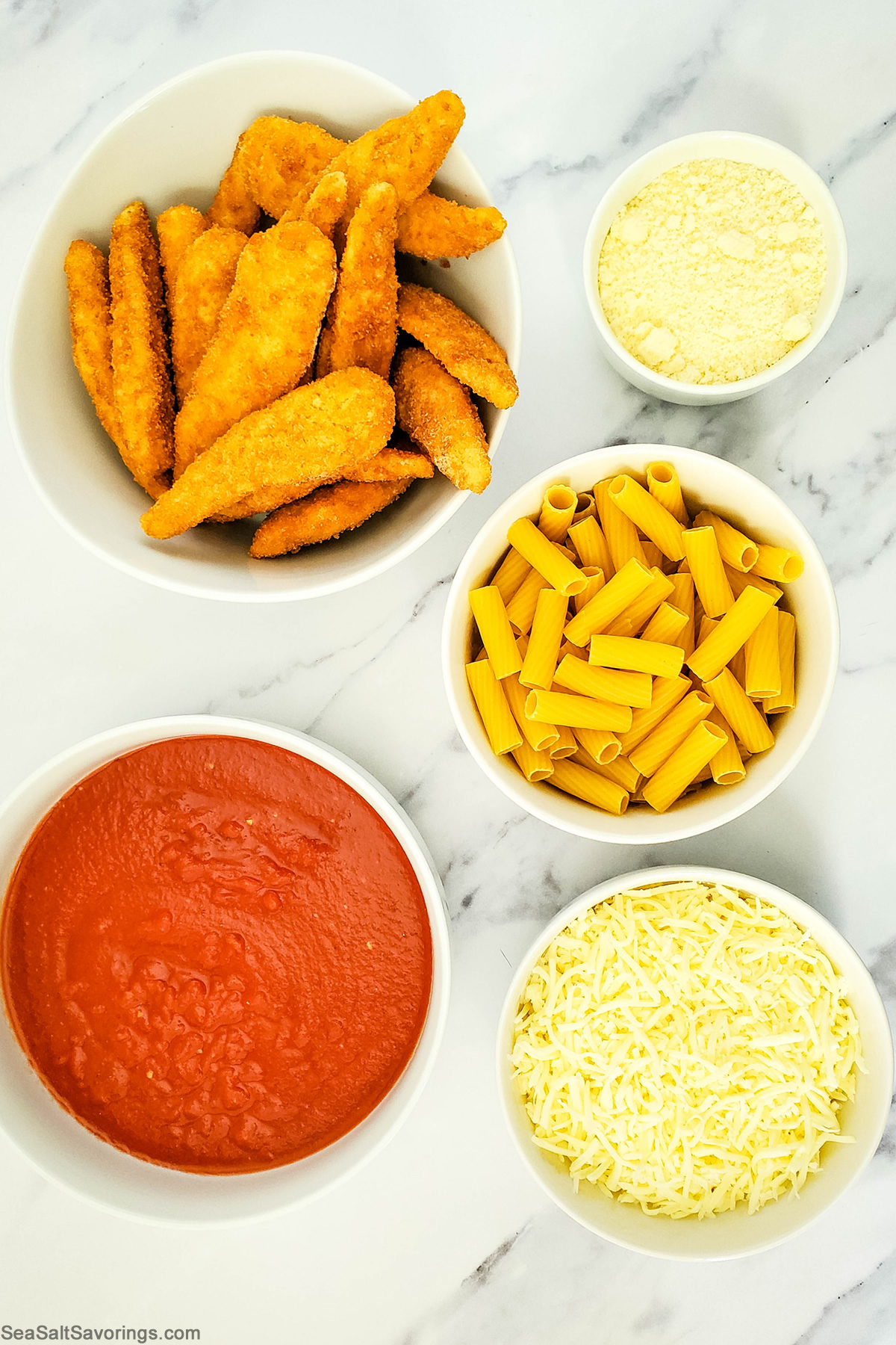 simple ingredients for chicken parmesan including chicken strips, noodles, cheese and red sauce