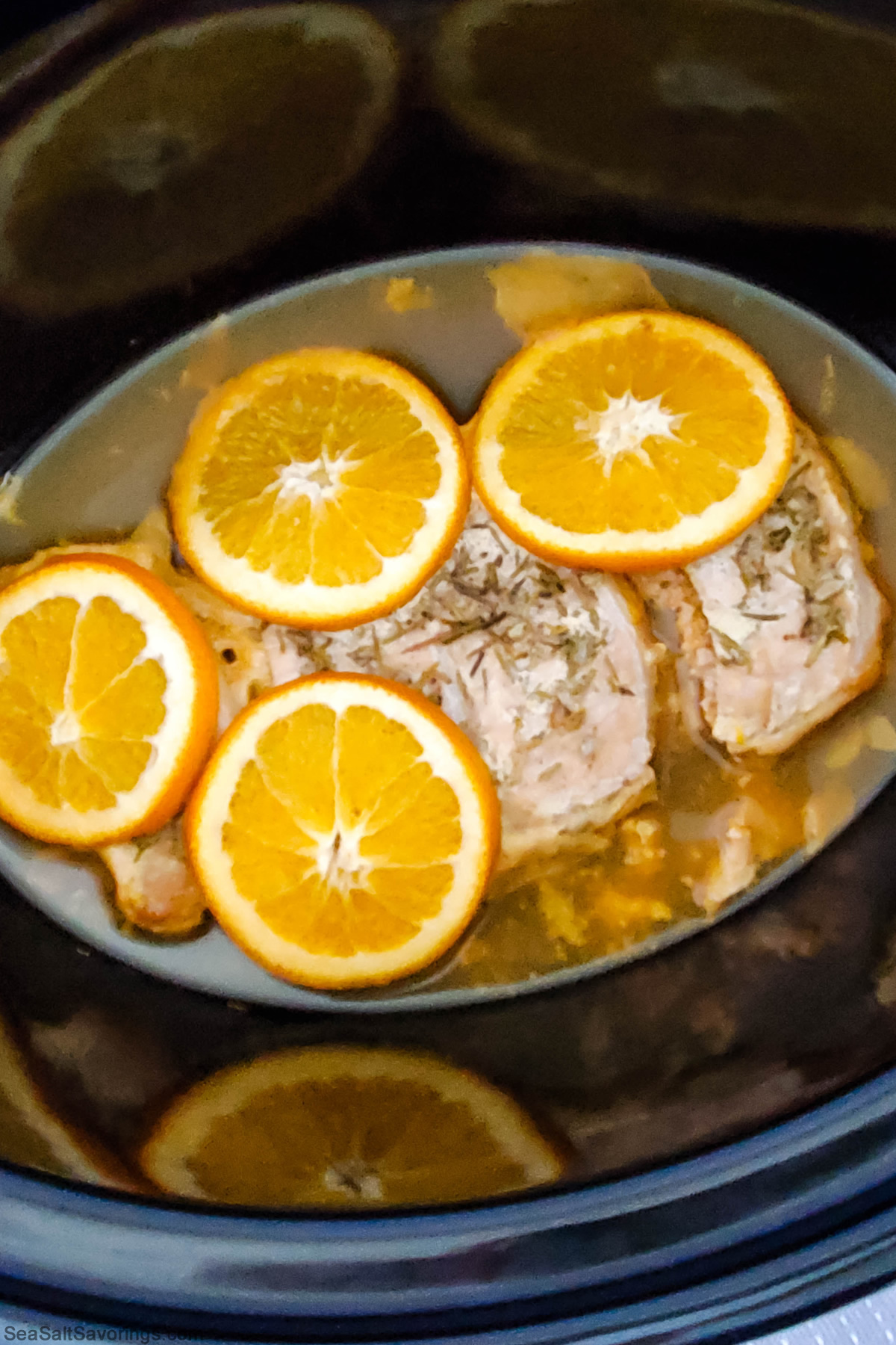 pork chops in a crock pot with sauce and season and slices of orange on top