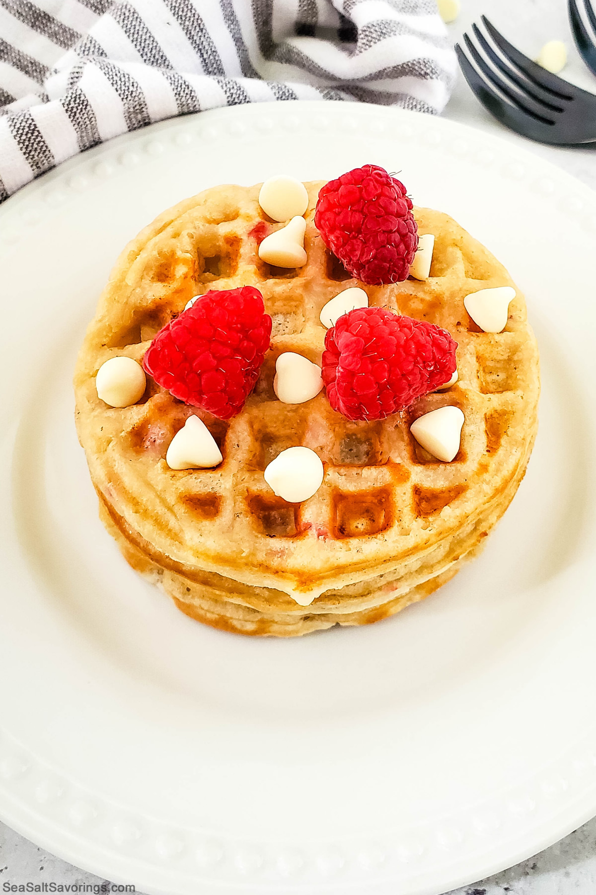 stack of waffles on a plate with raspberries and white chocolate pieces sprinkled on top