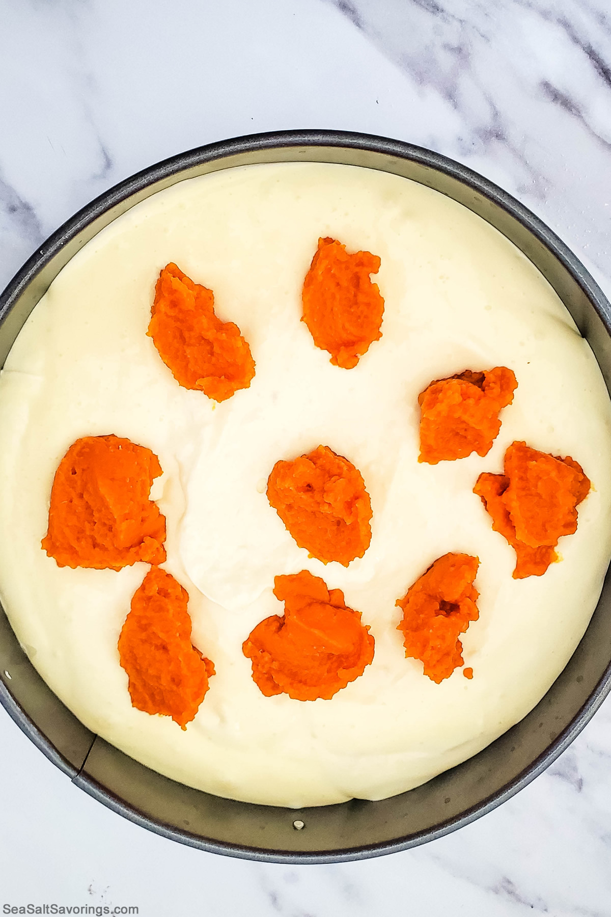 dropping spoonfuls of pumpkin puree onto top of cheesecake in baking pan