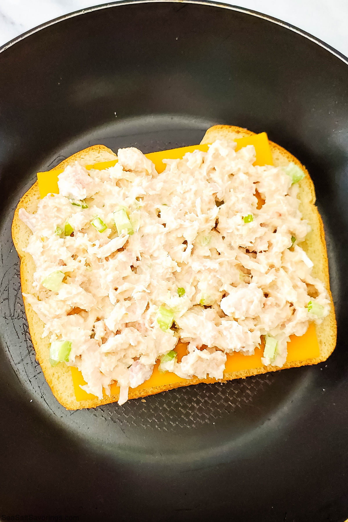 slice of bread laying on a frying skillet with tuna filling placed on top