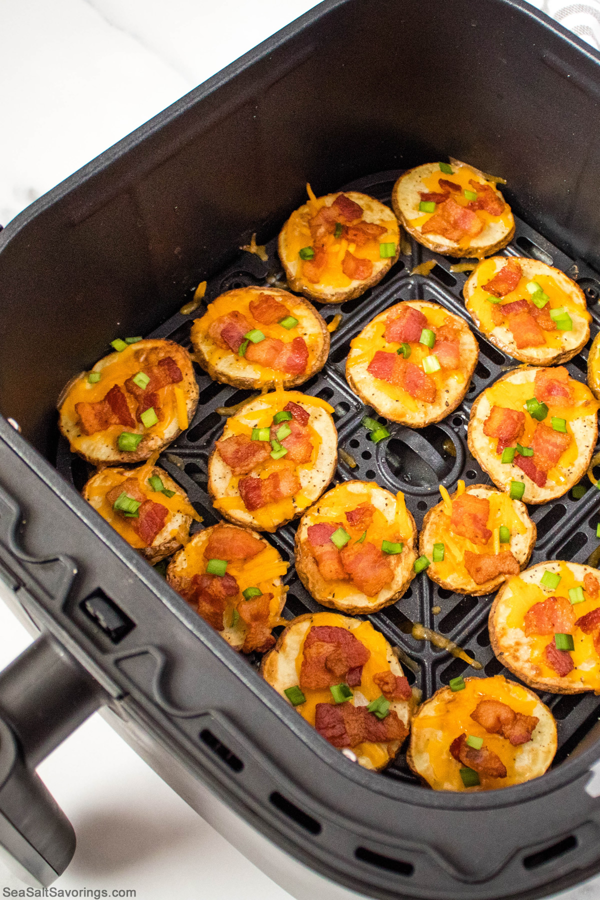 slices of potato in air fryer basket topped with cheese and bacon