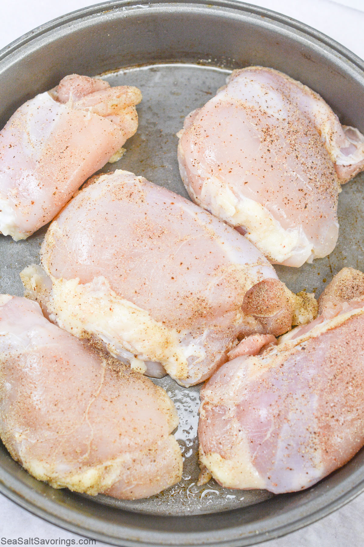 raw chicken thighs with season sprinkled on