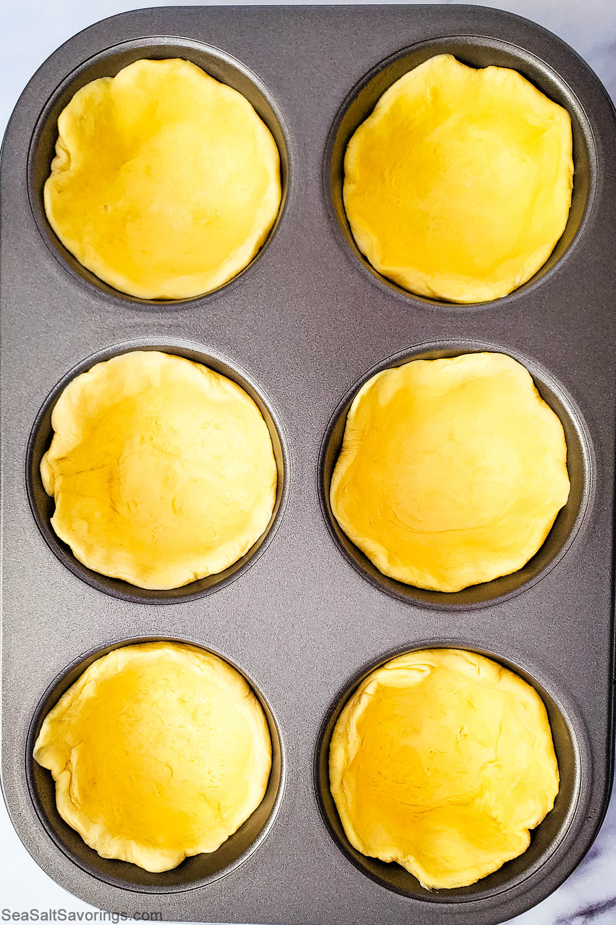 empty biscuits shaped into shells on a muffin baking dish