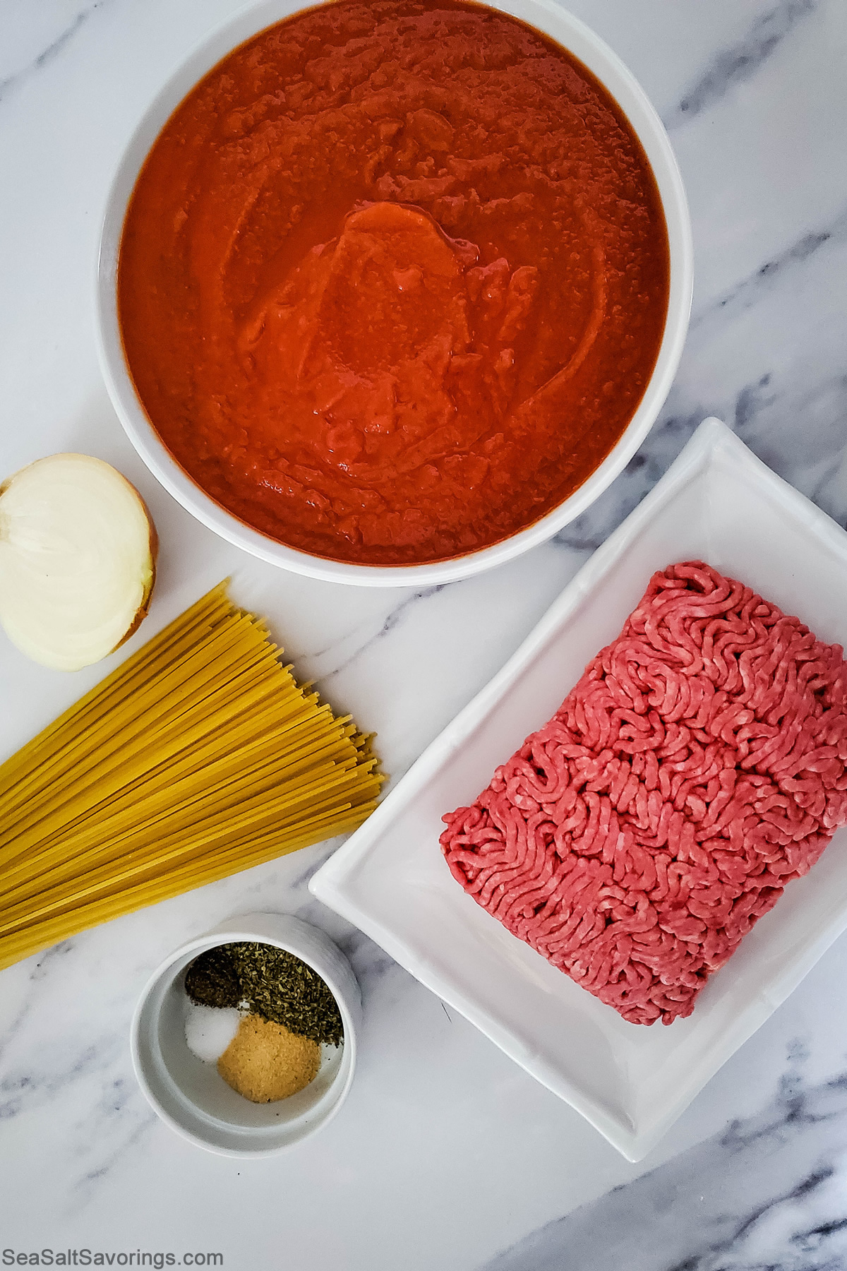 simple spaghetti ingredients on a table such as ground beef and tomato sauce and noodles and onion and seasoning