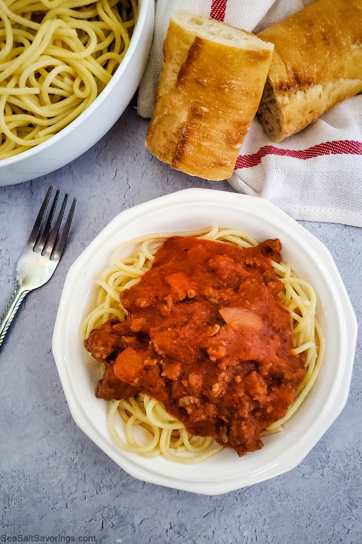 plate of spaghetti next to bowl of noodles and loaf of bread