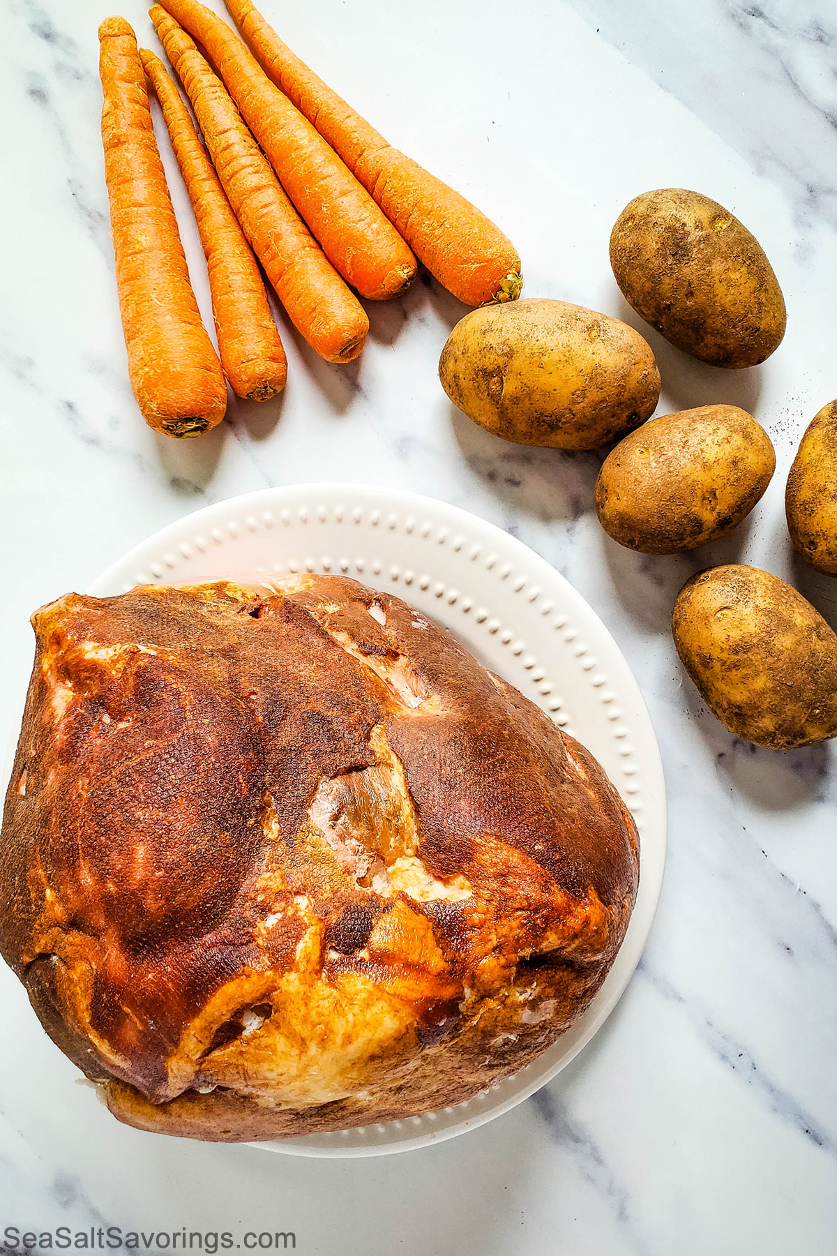 ingredients for a ham dinner including carrots and potatoes and a ham