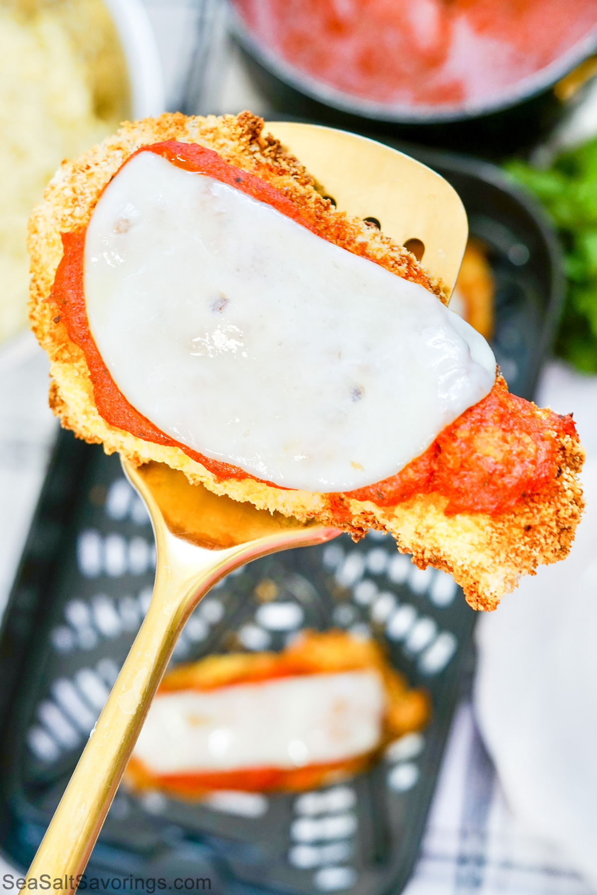 a chicken parmesan patty held up on a wooden spoon