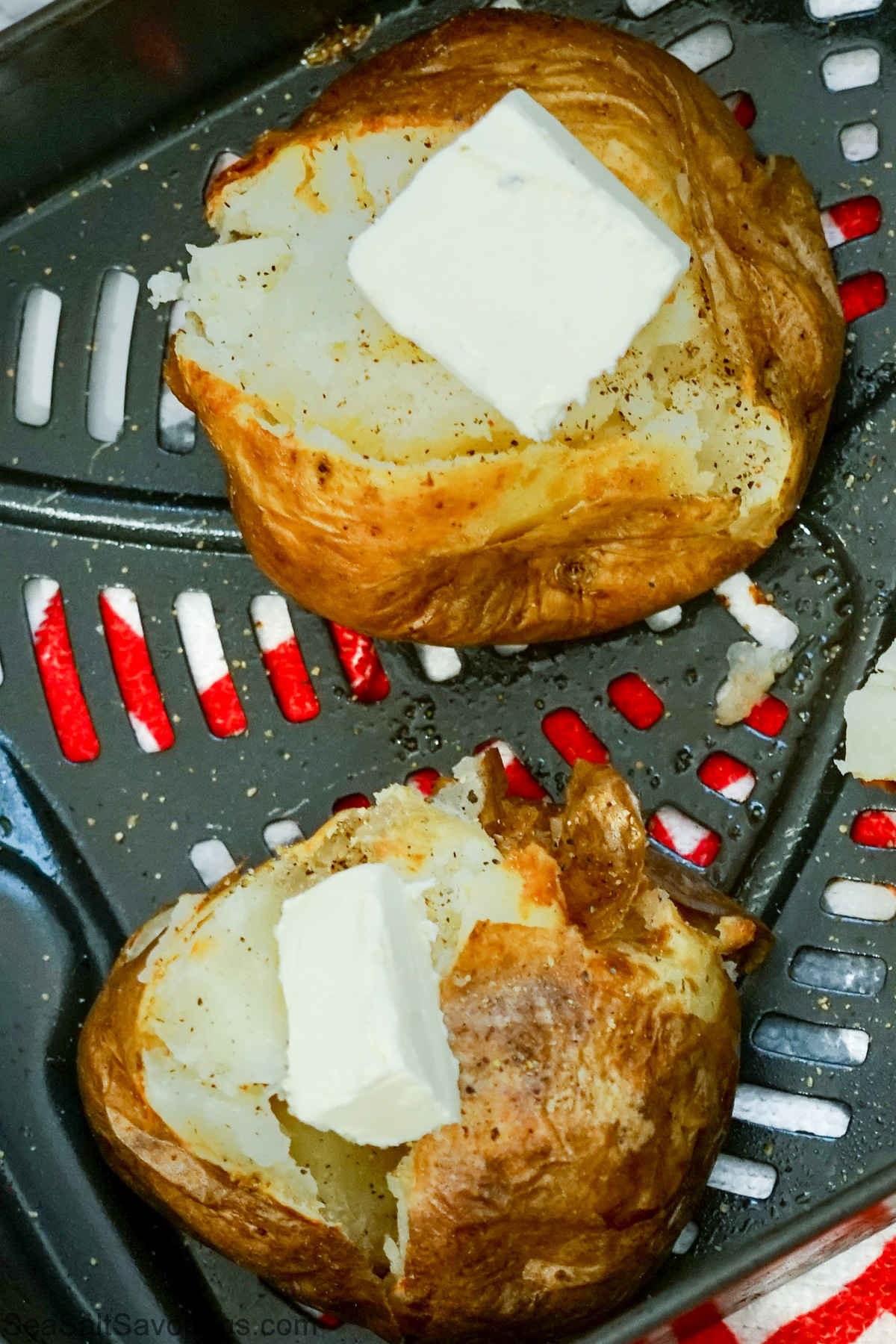 potatoes split open with butter and season sprinkled on in an air fryer basket