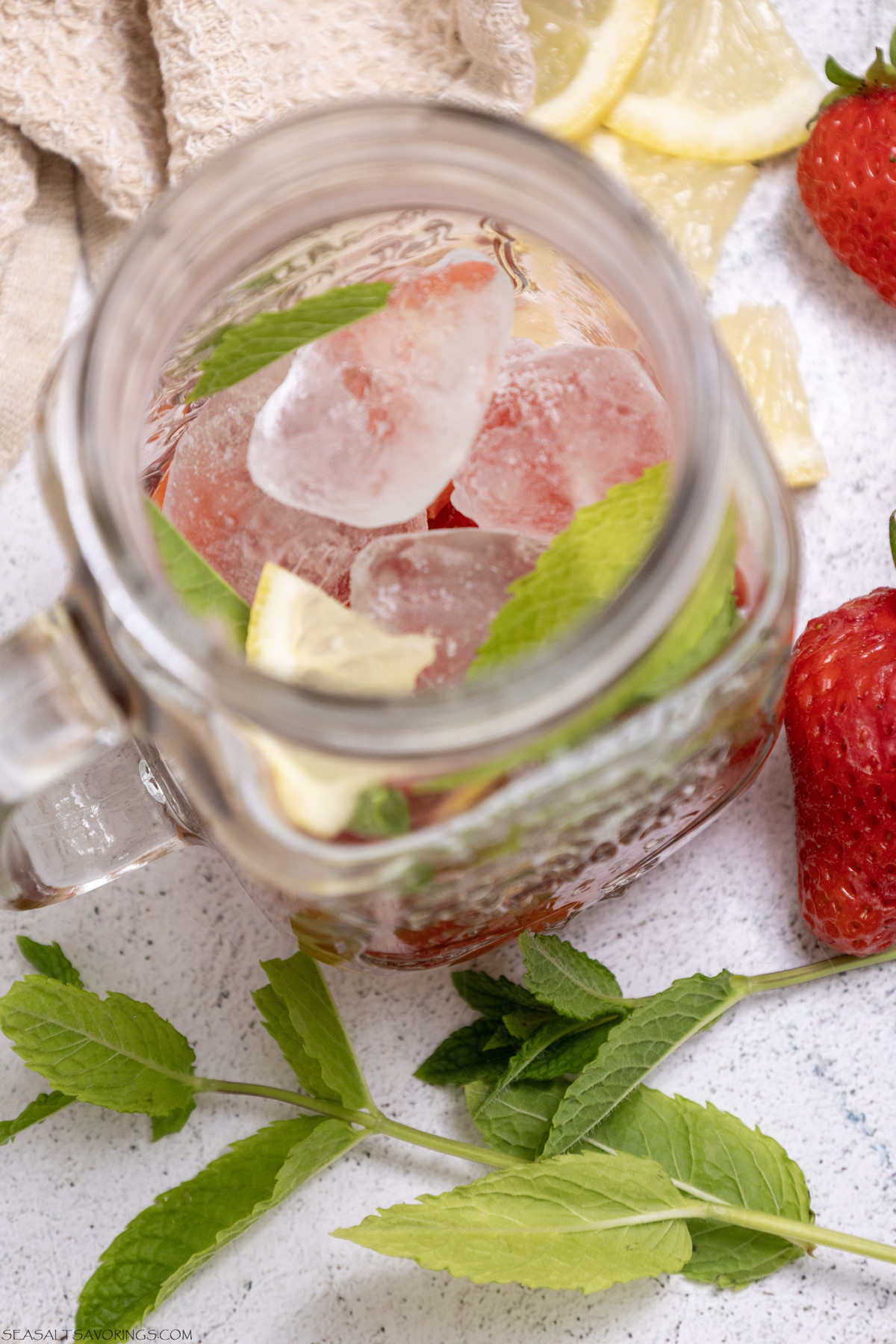 adding strawberries, lemon, mint and ice to a jar