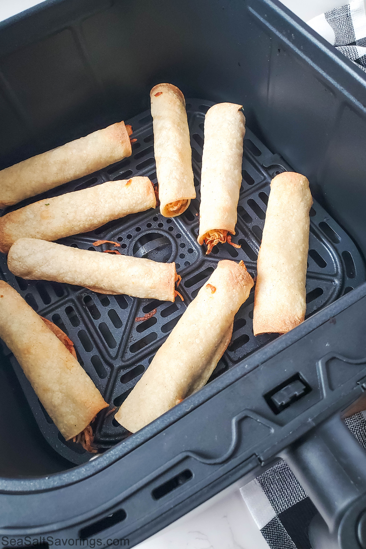 air fryer basket with cooked taquitos inside