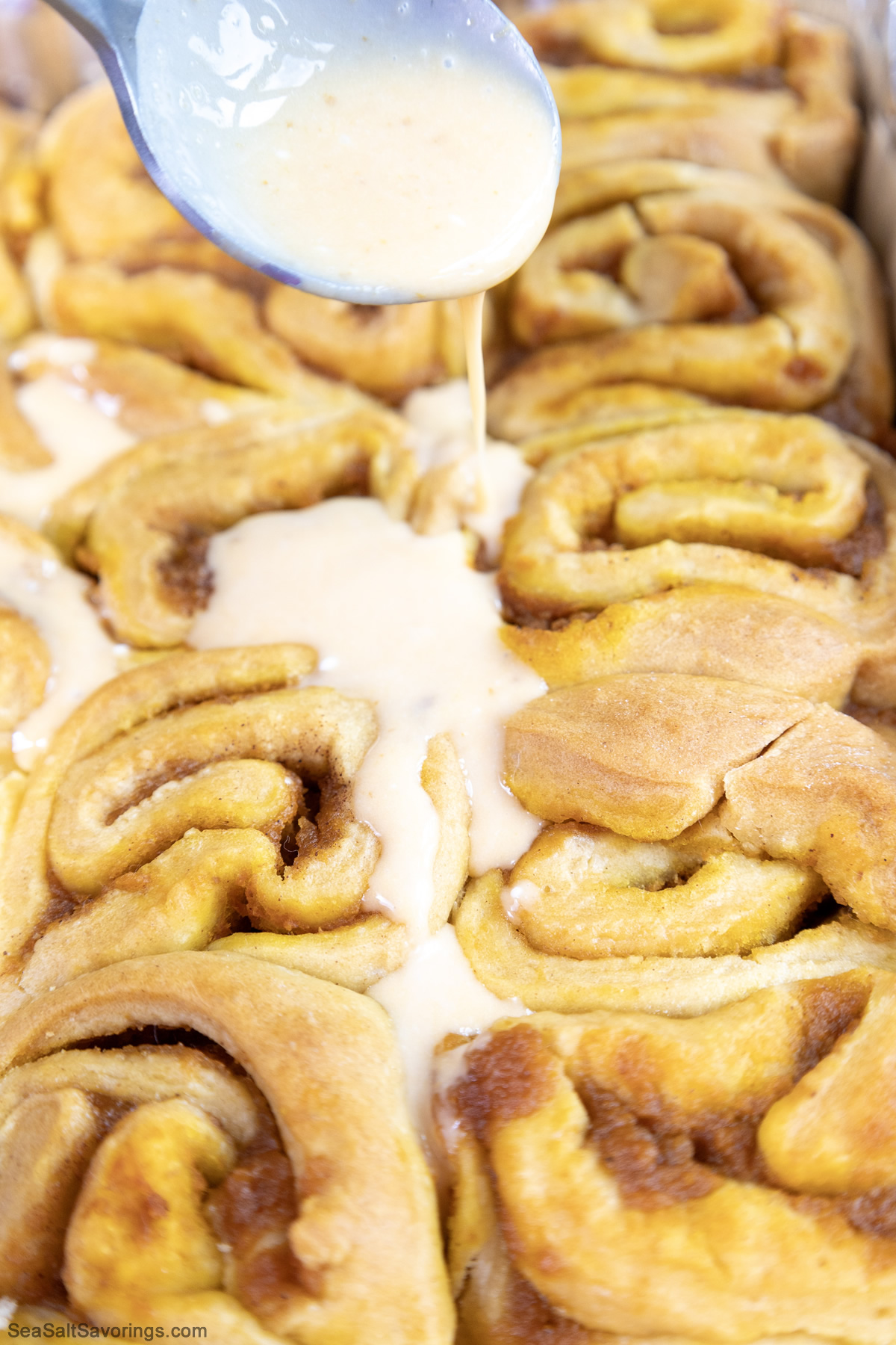 spoon drizzling frosting on cooked cinnamon rolls
