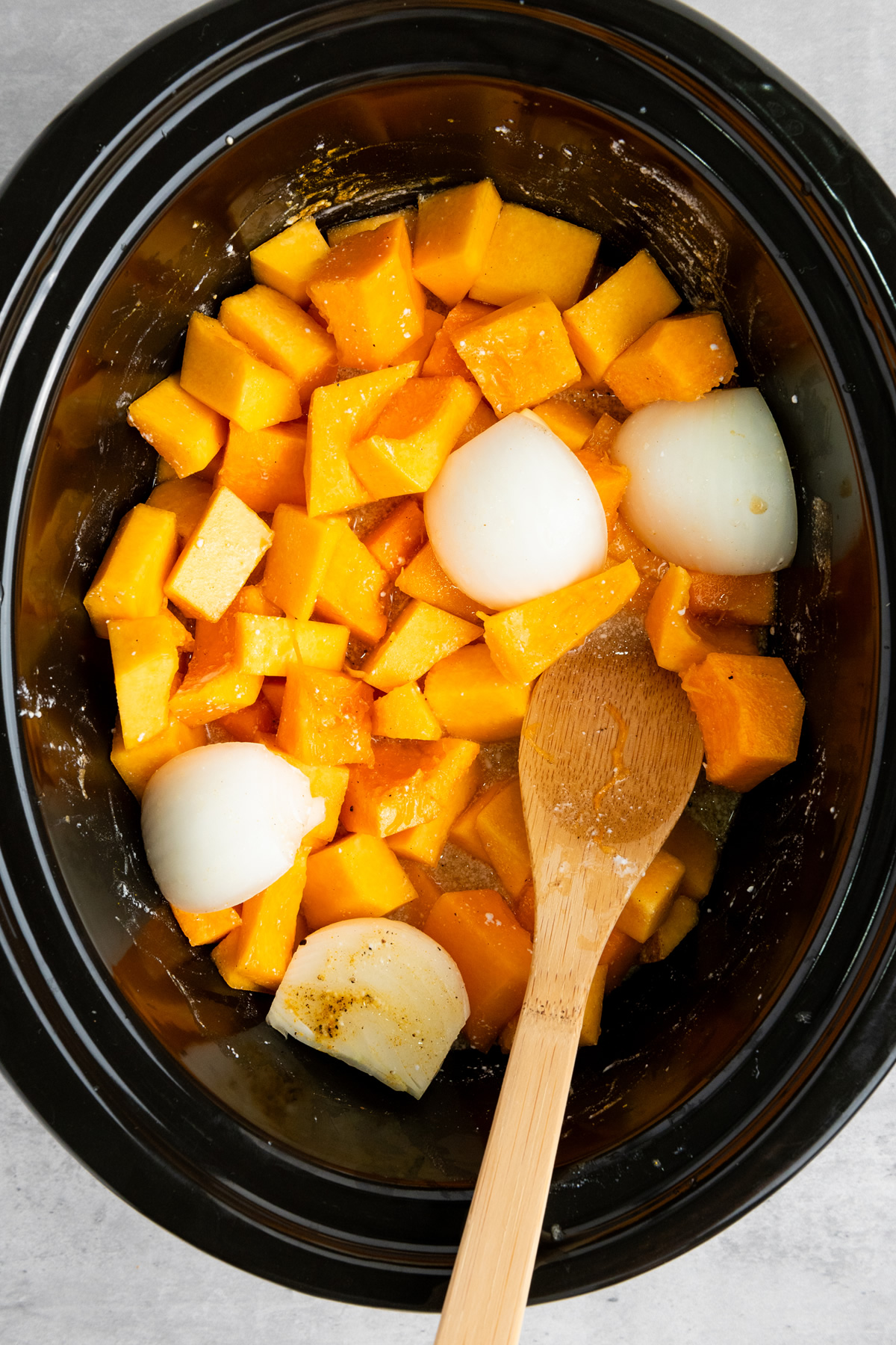 squash soup ingredients in slow cooker getting mixed with wooden spoon