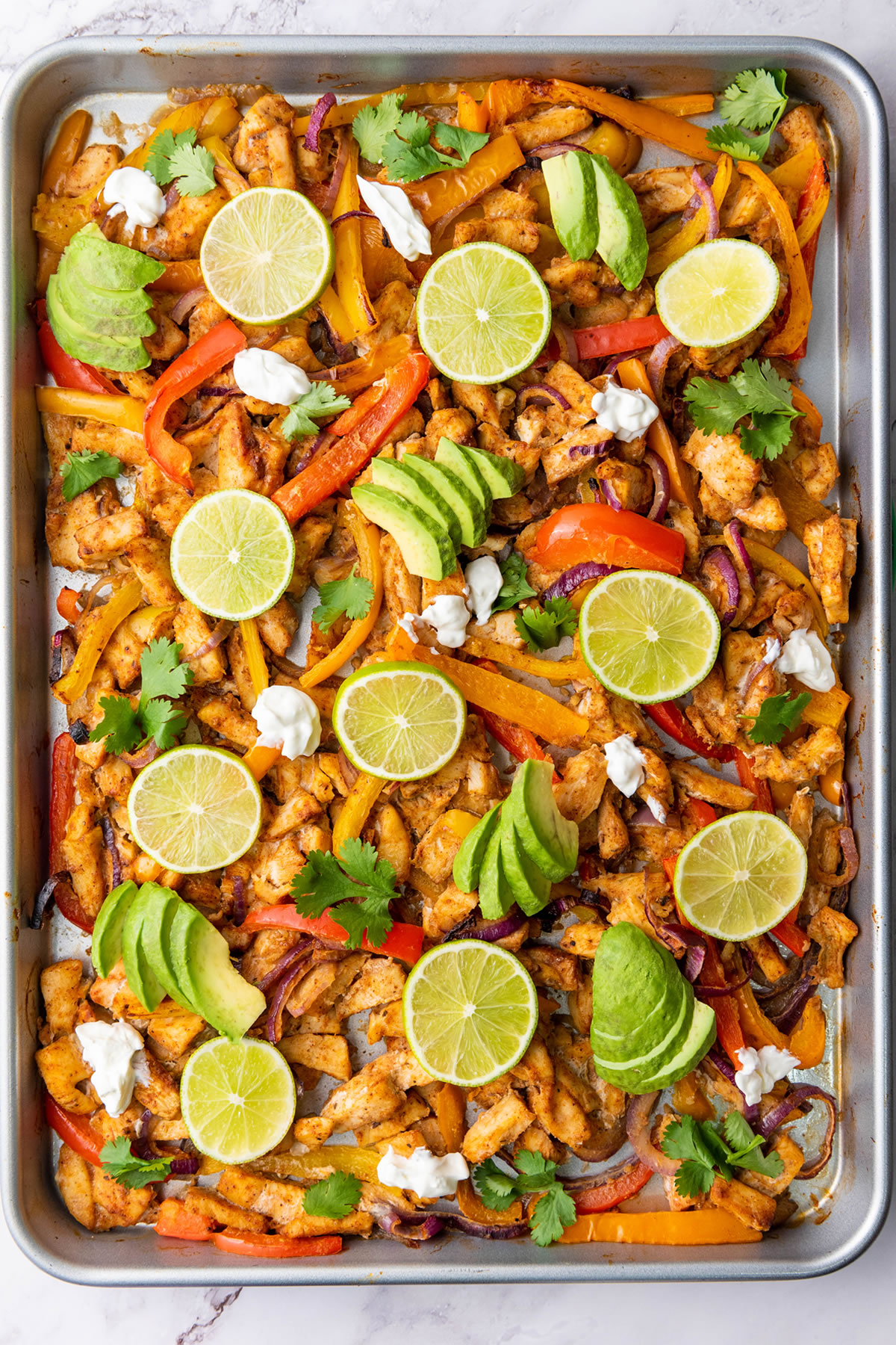 sheet pan with spread of seasoned chicken and fresh vegetable toppings