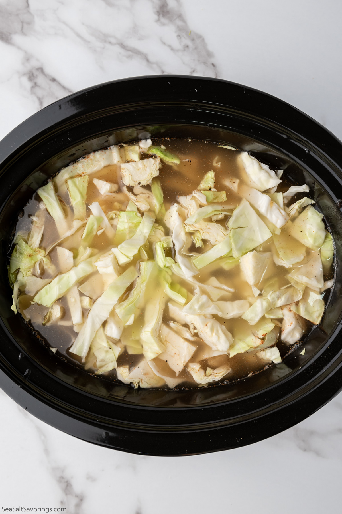 all ingredients in a crockpot with cabbage floating on top