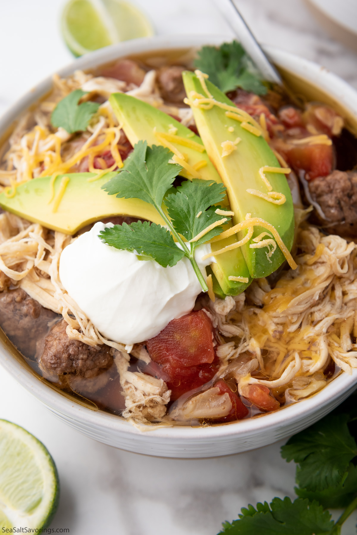 Taco Soup garnished with avocado, lime, cilantro, sour cream, and shredded cheese, served hot