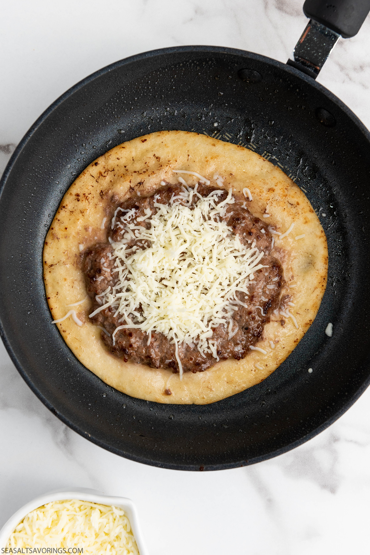 tortilla in a pan cooking with beef patty and cheese on top