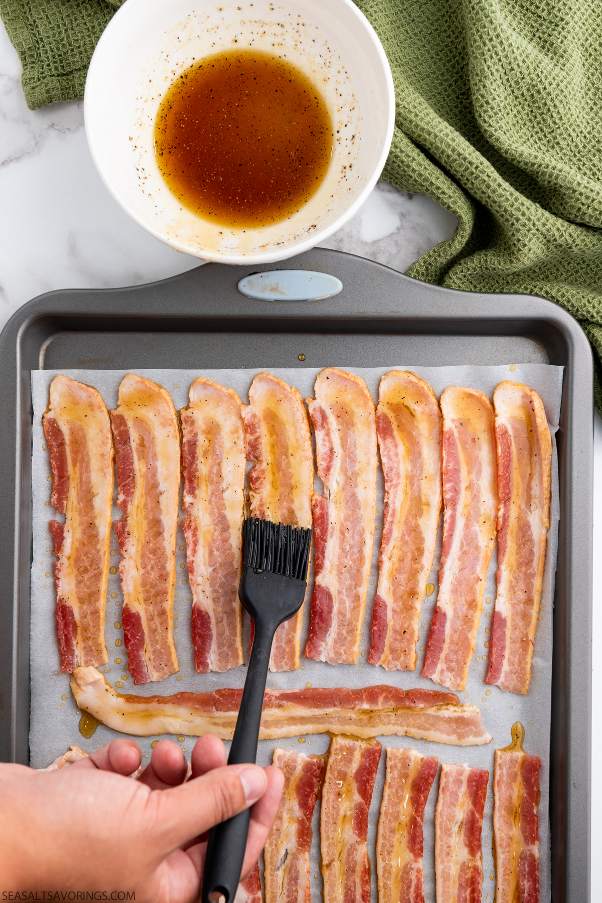 brushing sauce onto bacon strips on a pan