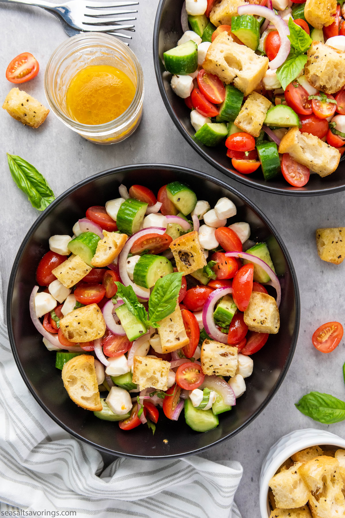 overhead view of two bowls of panzanella salad with brightly colored vegetables and cubes of ciabatta