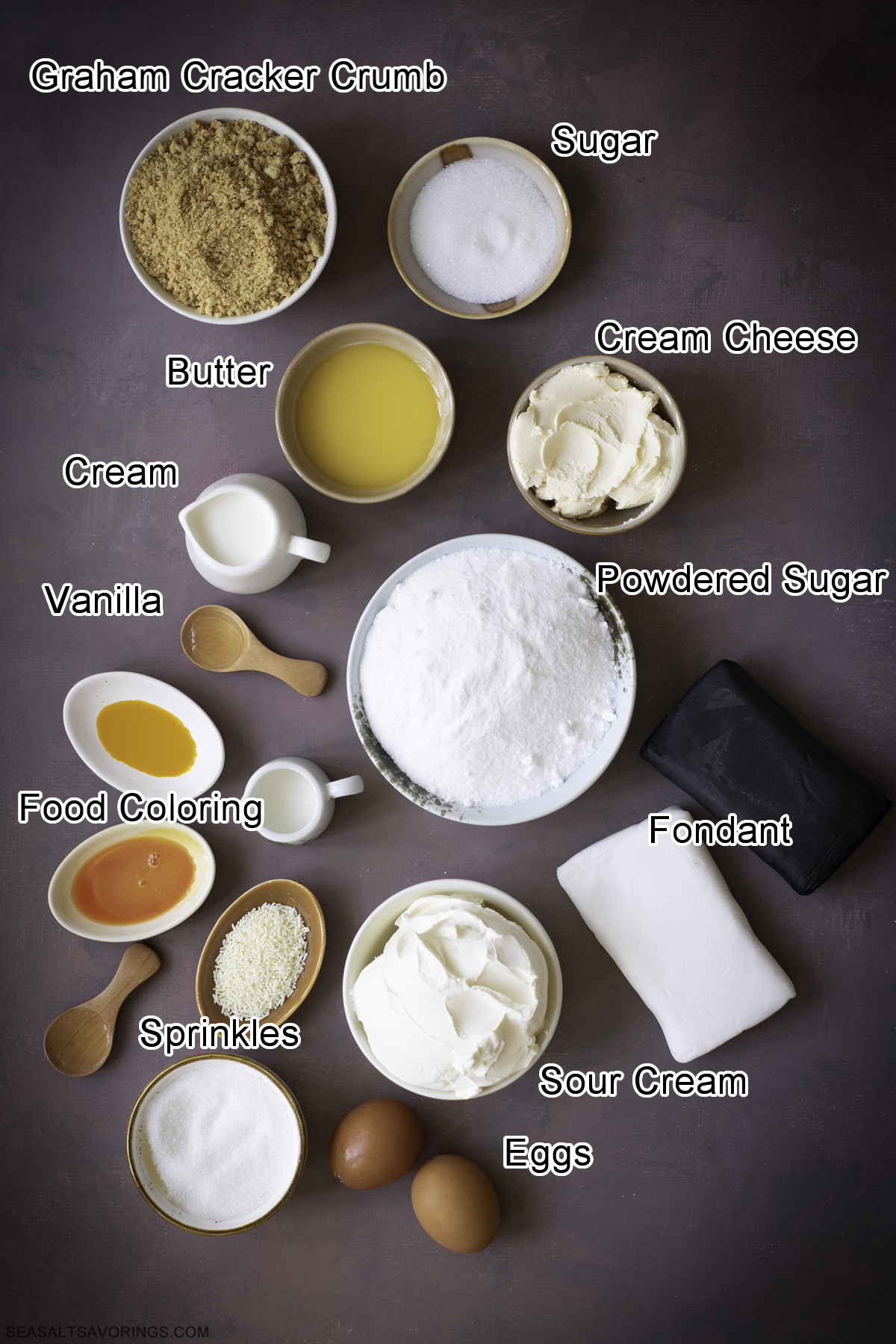 recipe ingredients on a table for the mini cheesecakes, it includes bowls of graham cracker crust, sugar, cream cheese, powdered sugar and more