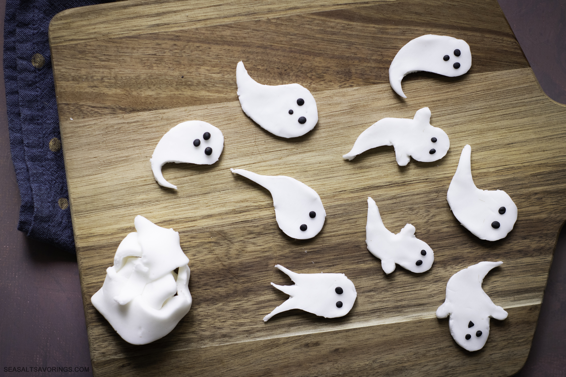 the fondant ghosts finished being cut out of the sheet of fondant, with small black balls of fondant placed for eyes