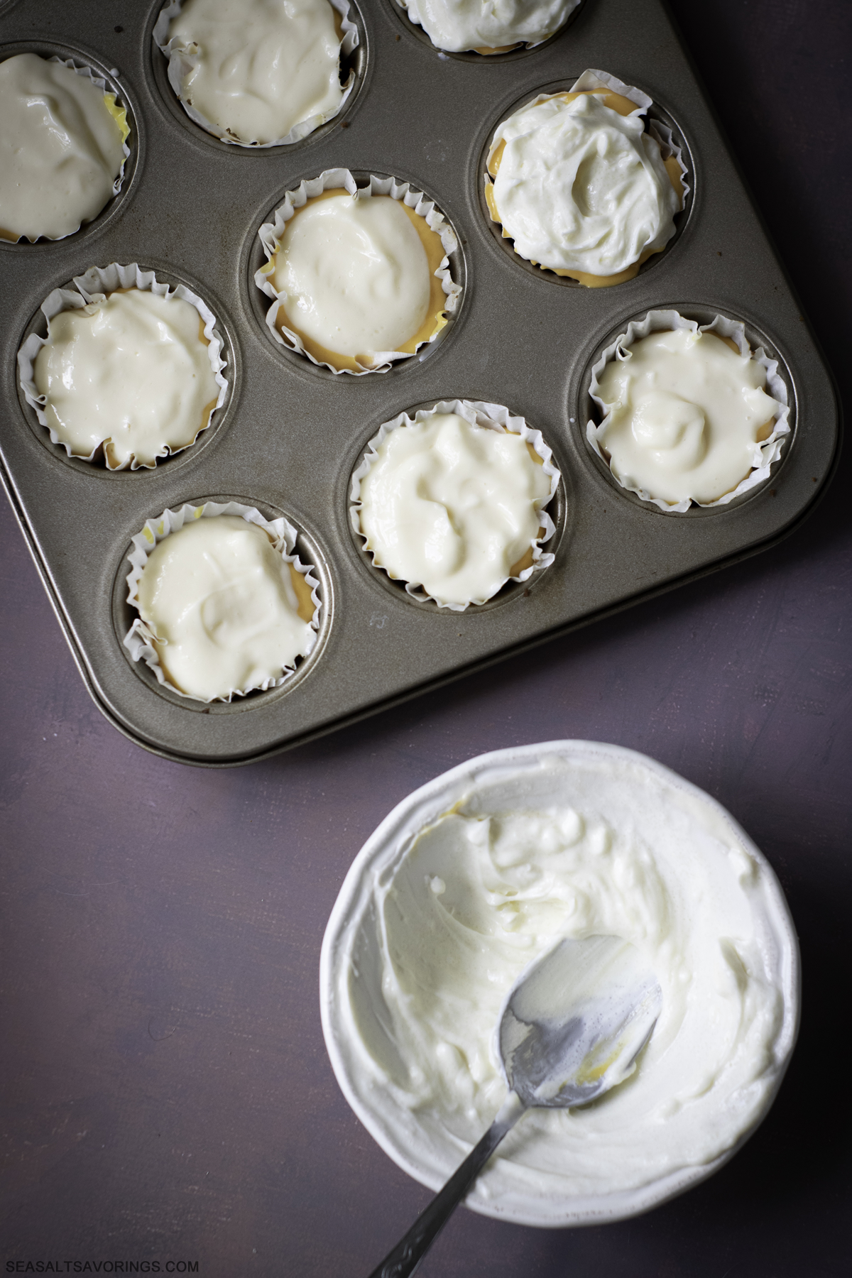 scooping the final layer of batter into the cupcake liners that are filled with batter and graham cracker crumble crust