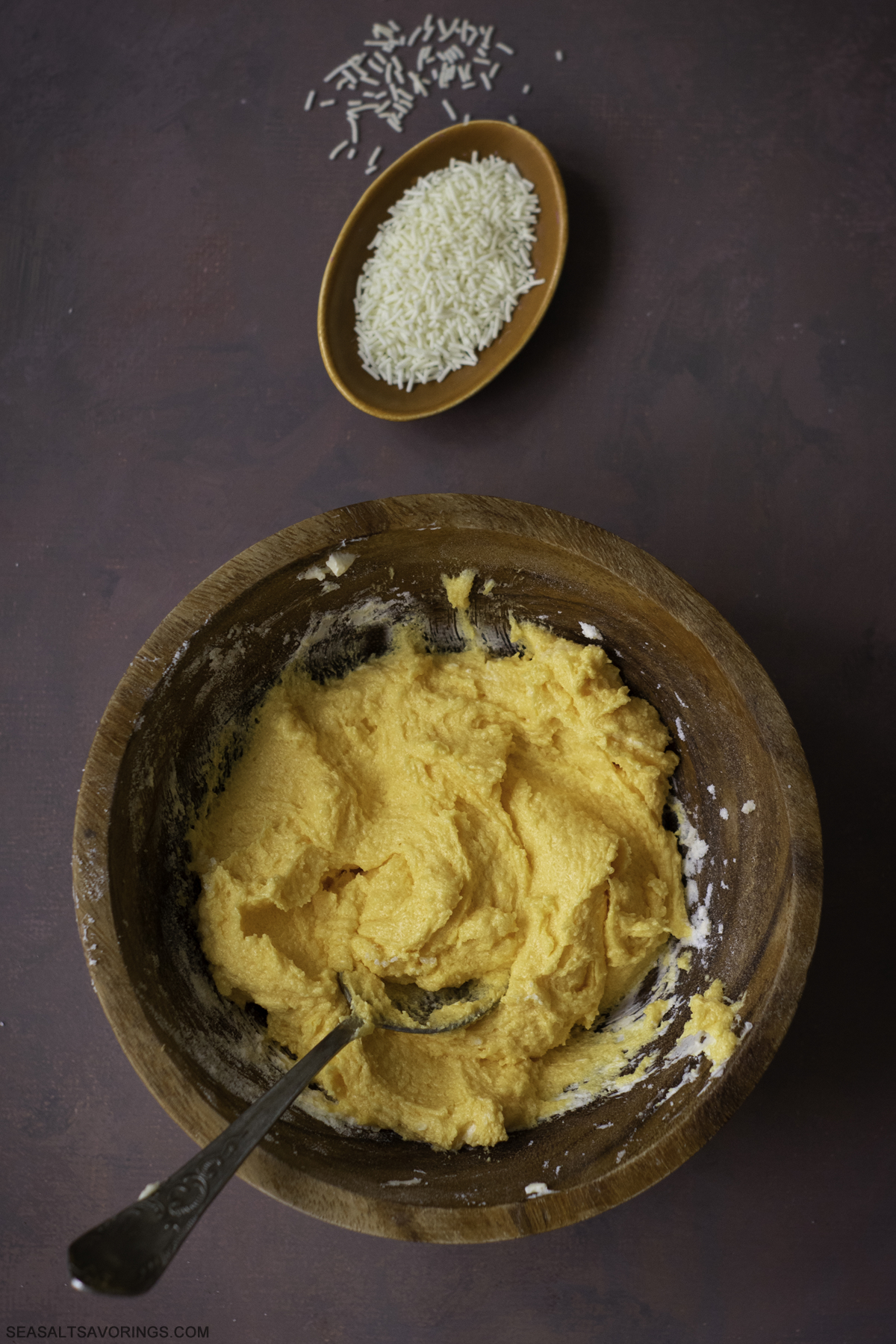 mixing bowl of orange frosting next to a smaller bowl of sprinkles