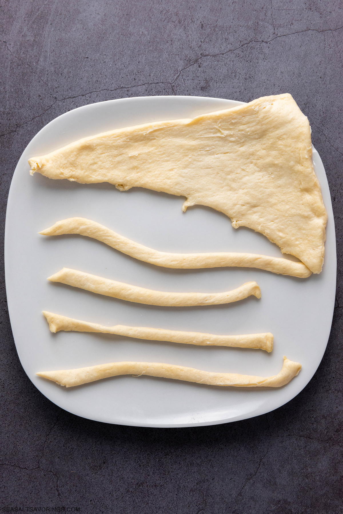 crescent roll dough on a plate detailing that its getting cut into ropes