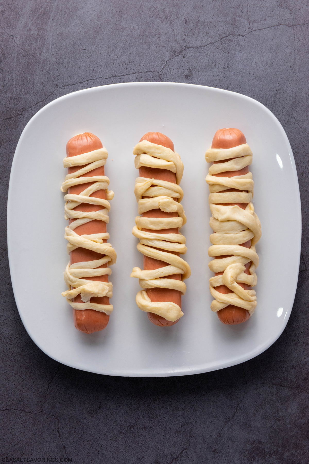 the hot dogs on a plate and wrapped with the strings of crescent roll dough