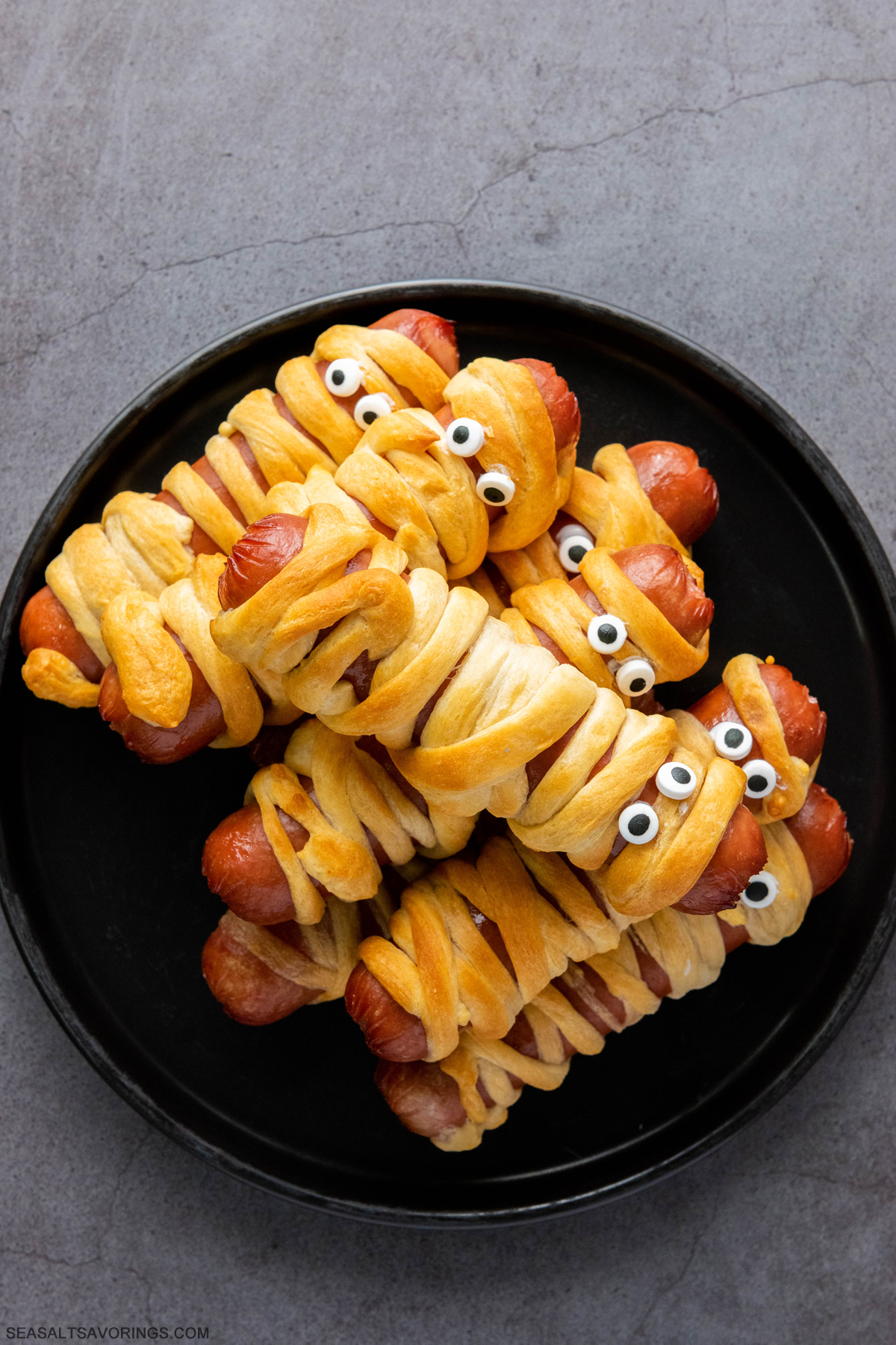 plate of hot dogs wrapped in baked crescent rolls with googly eyes to mimic appearance of a mummy