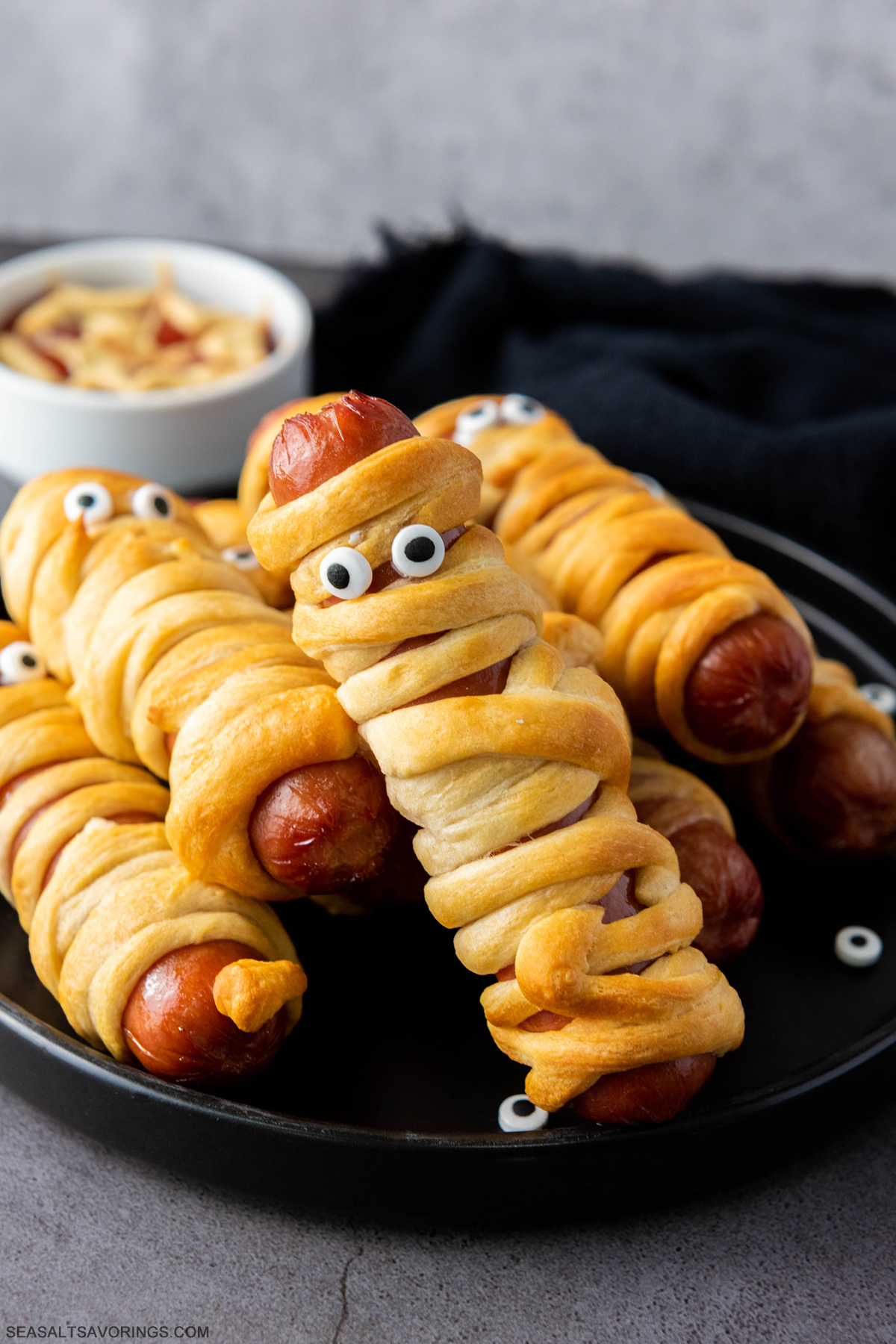 plate of hot dogs wrapped in baked crescent rolls with googly eyes to mimic appearance of a mummy