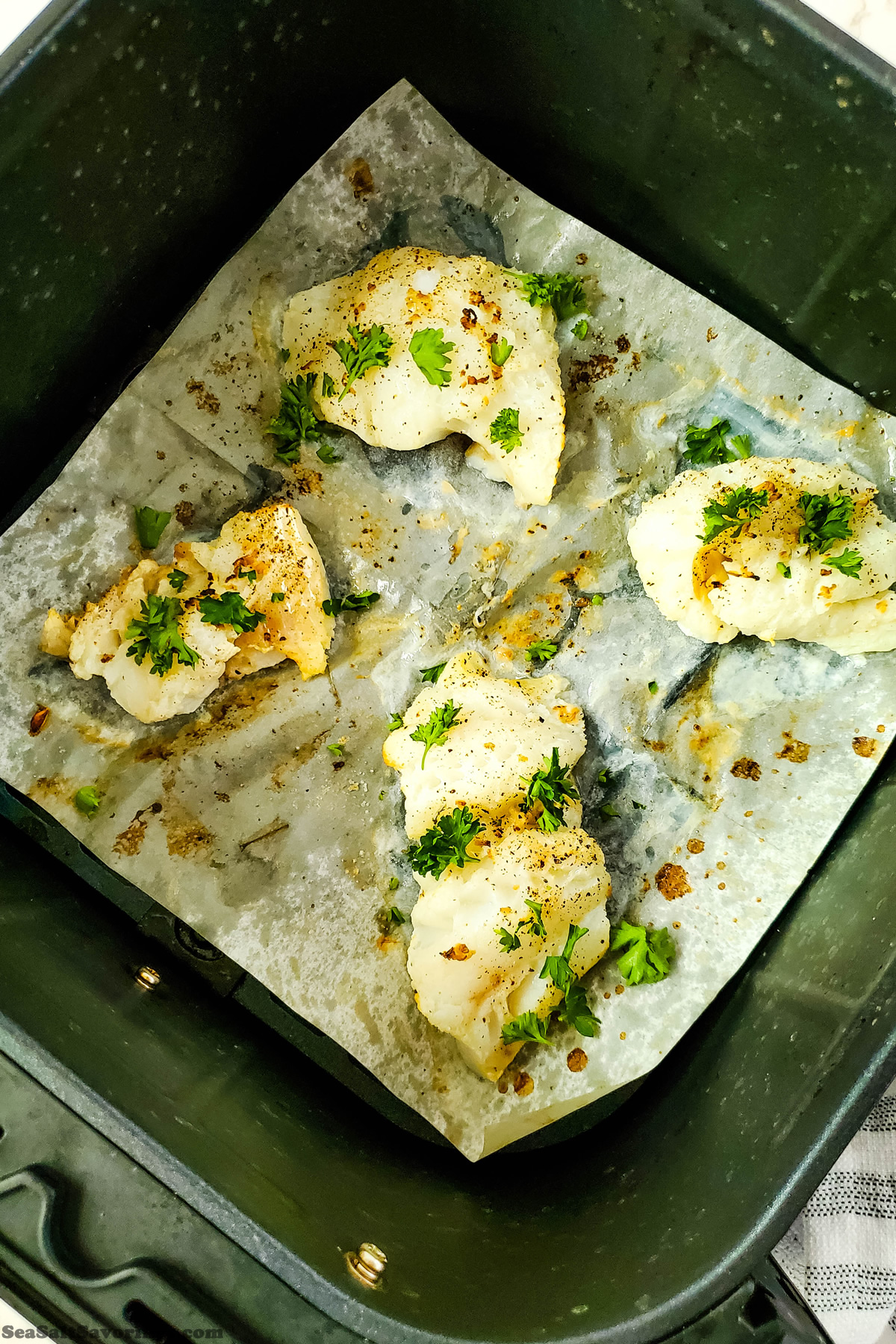 four cooked cod filets with garnish in air fryer basket