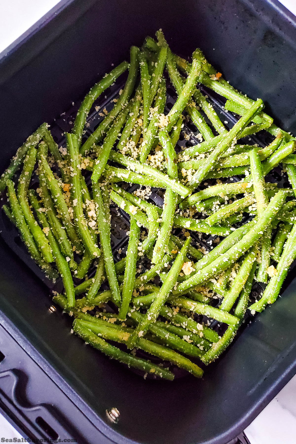 coated fresh green beans in a single layer of an air fryer basket