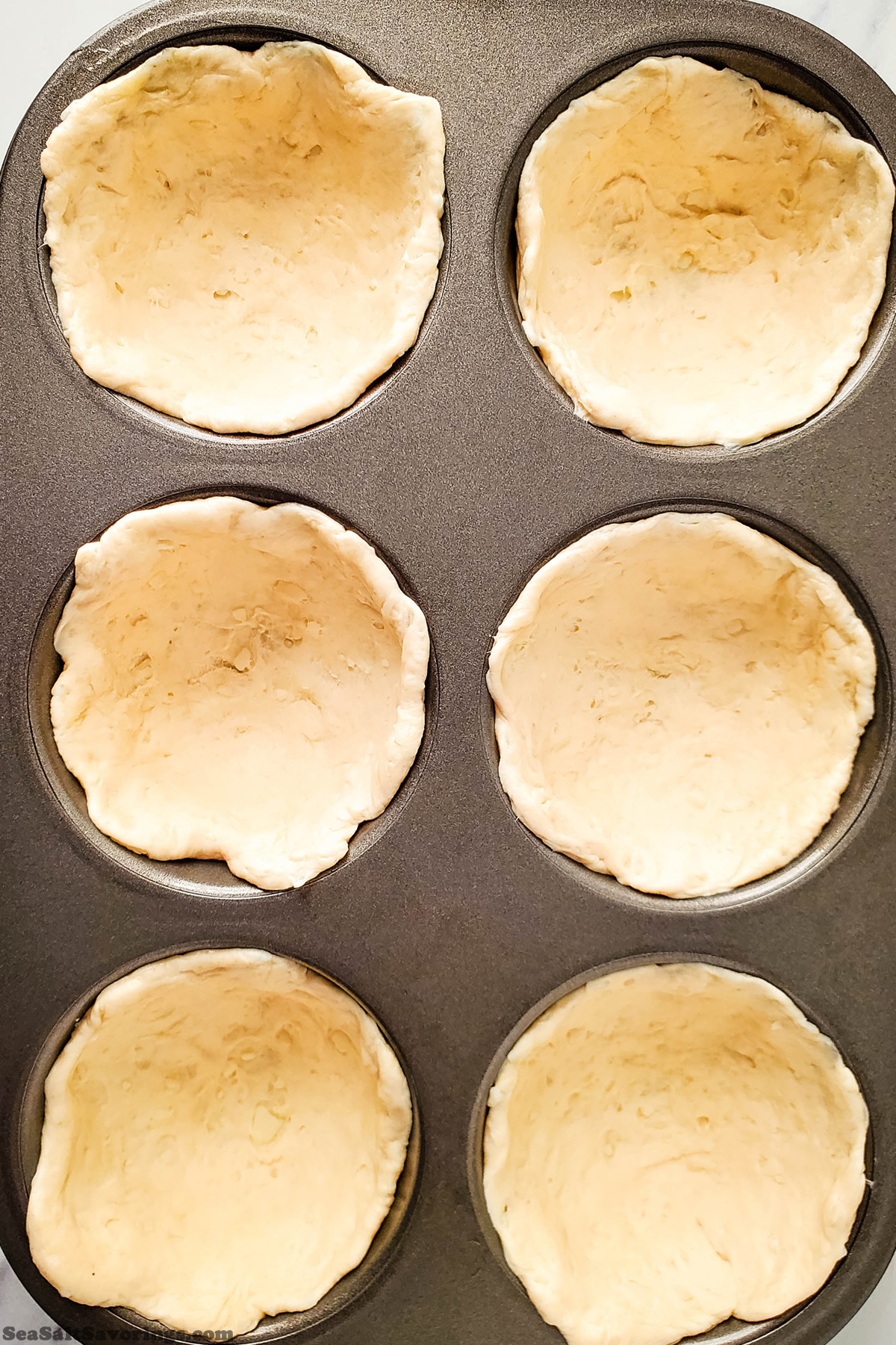 muffin baking pan with biscuit dough placed and form at bottom to form cups