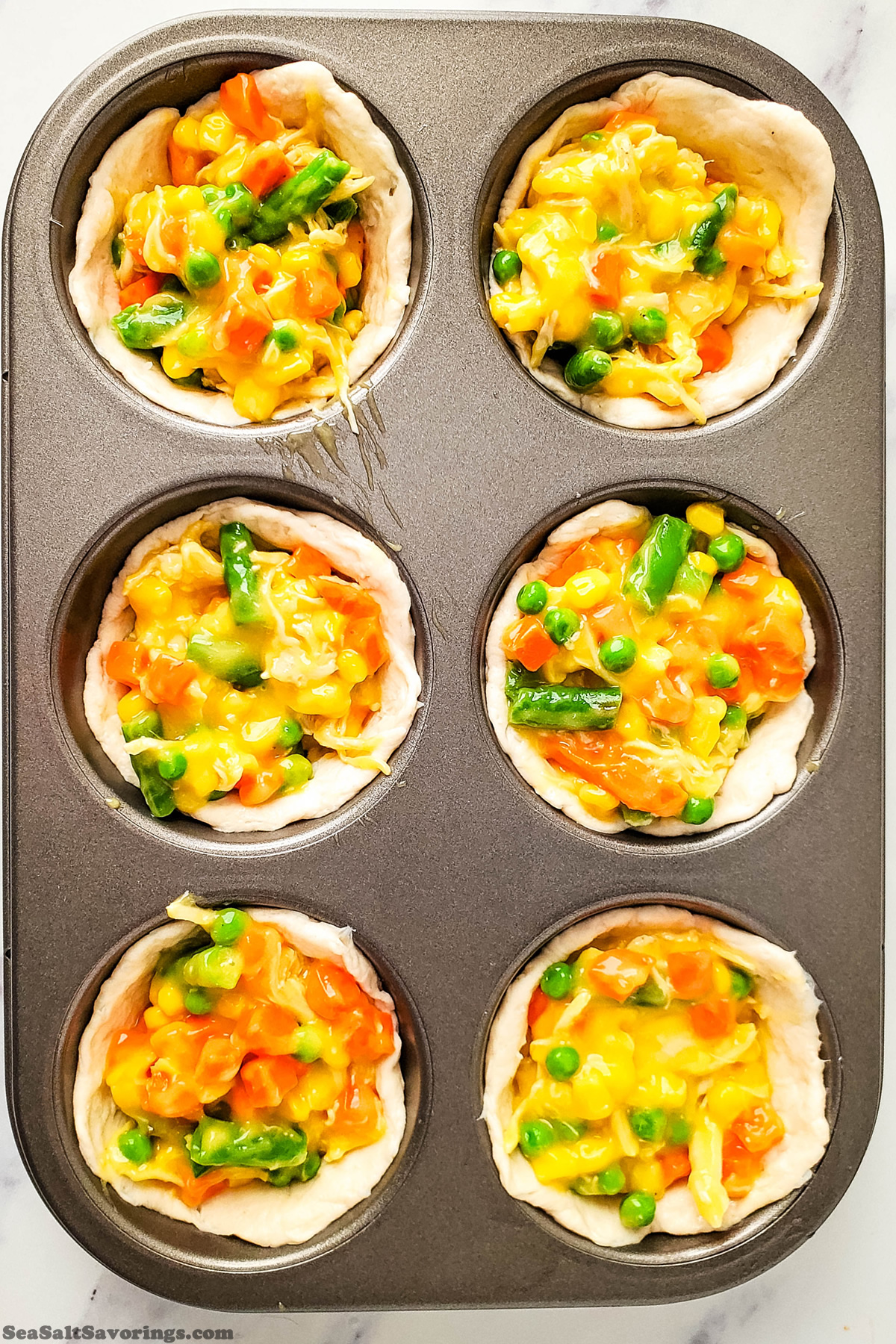 muffin baking dish with dough filled with vegetable cheese and chicken mixture