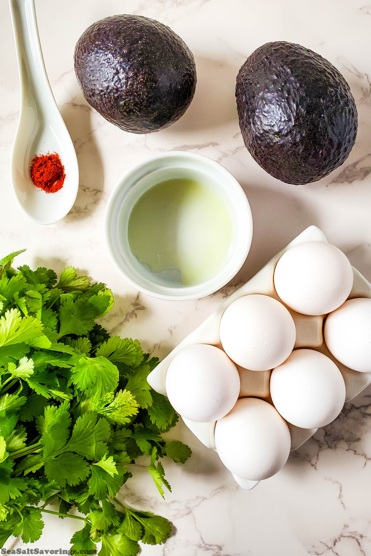 simple ingredients for avocado deviled eggs on a table such as avocados, eggs, oil and garnish