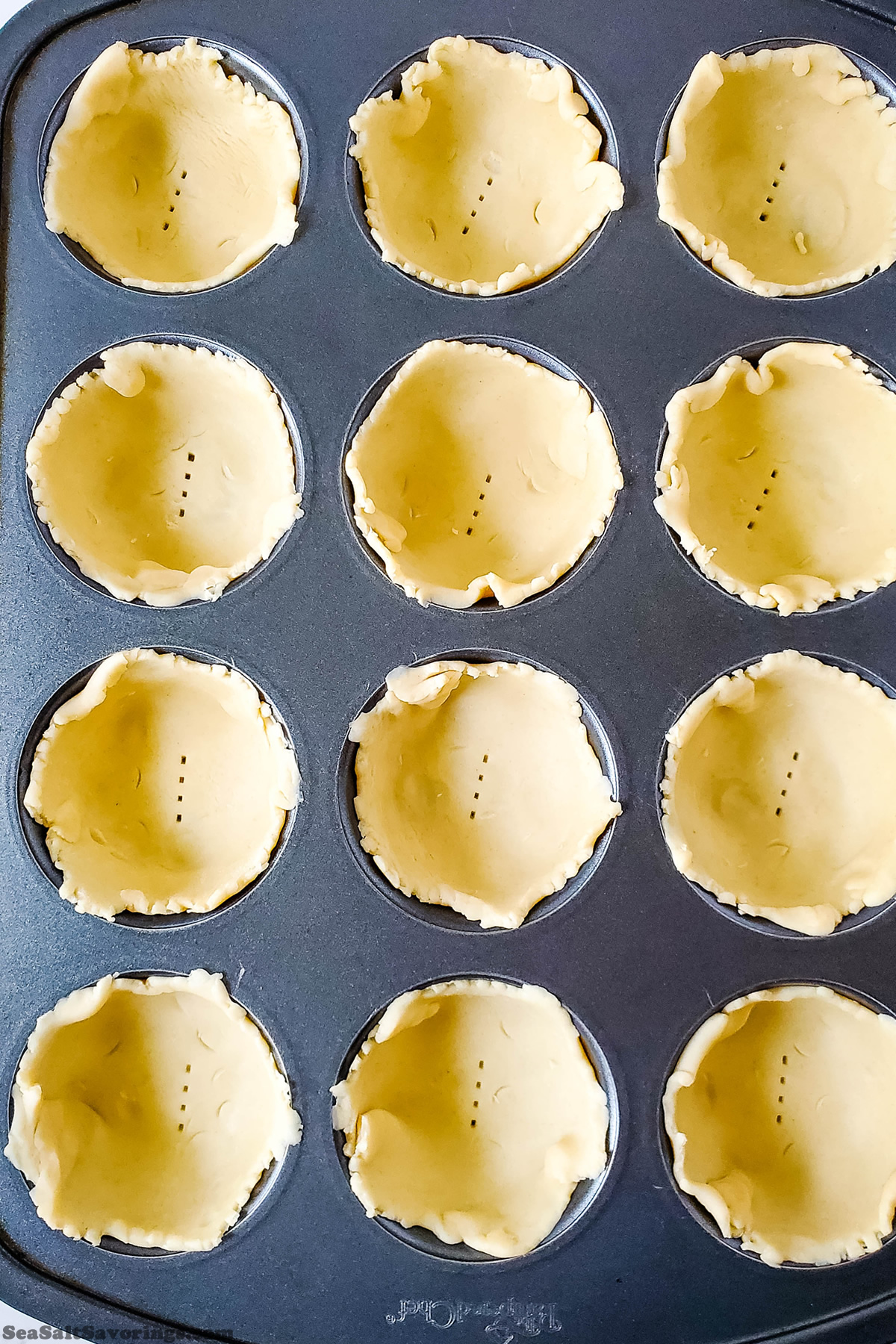 cupcake baking tin with pie dough pieces placed and formed into cups and holes poked in the bottom