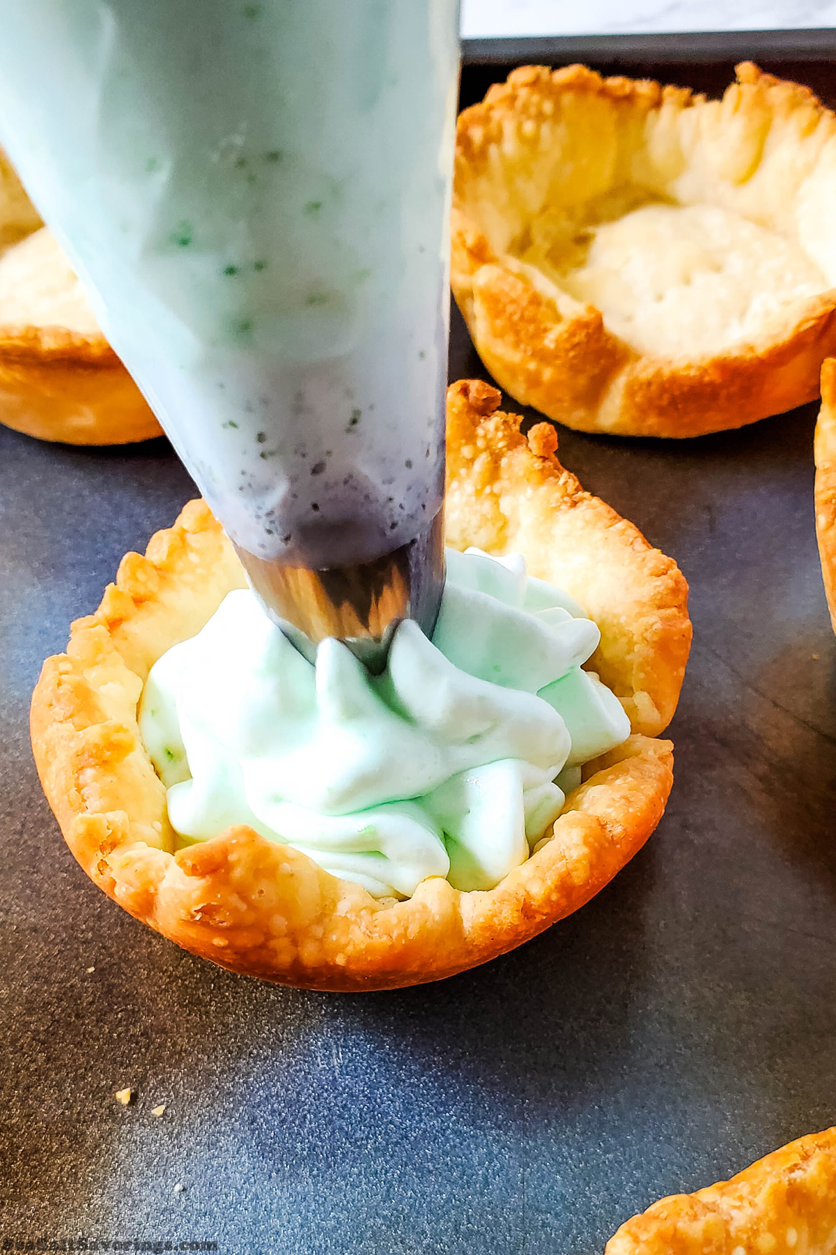 piping bag with filling mixture getting inserted into cooked pie shells