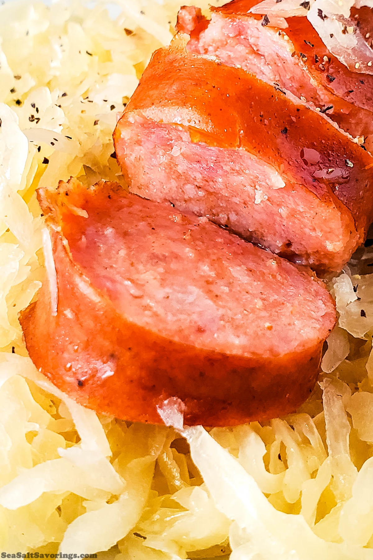 close up view of a kielbasa sausage laying on a bed of sourkraut, showing the details of textures and ingredients